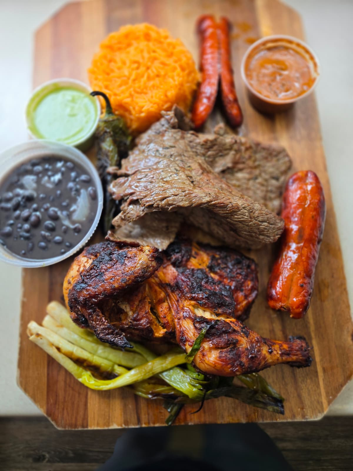 Mixed grill platter with grilled chicken, steak, sausages, black beans, orange rice, roasted jalapeño, scallions and sauces