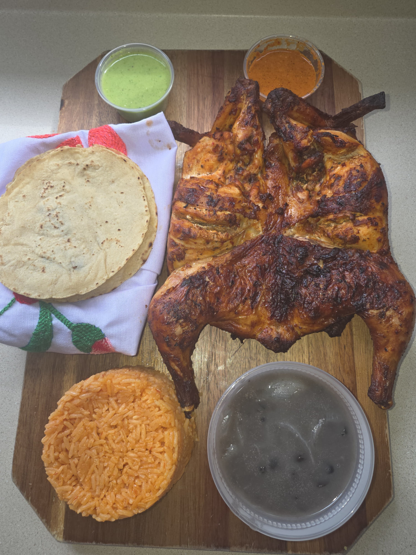 Whole grilled chicken with tortillas, orange rice, beans and green and red sauces
